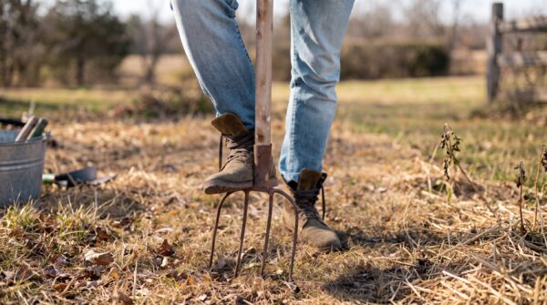 personne en train de planter sa fourche dans le sol pour l'aérer