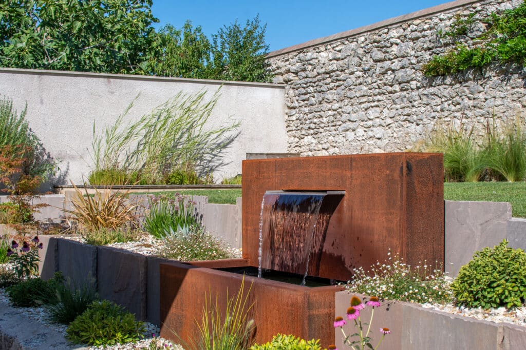 Fontaine Fontaine en acier corten rouge au milieu d'un jardin paysager