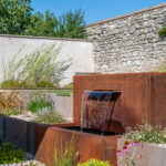 Fontaine en acier corten rouge au milieu d'un jardin paysager
