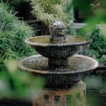 Fontaine dans un jardin sur un bassin entouré de plantes.